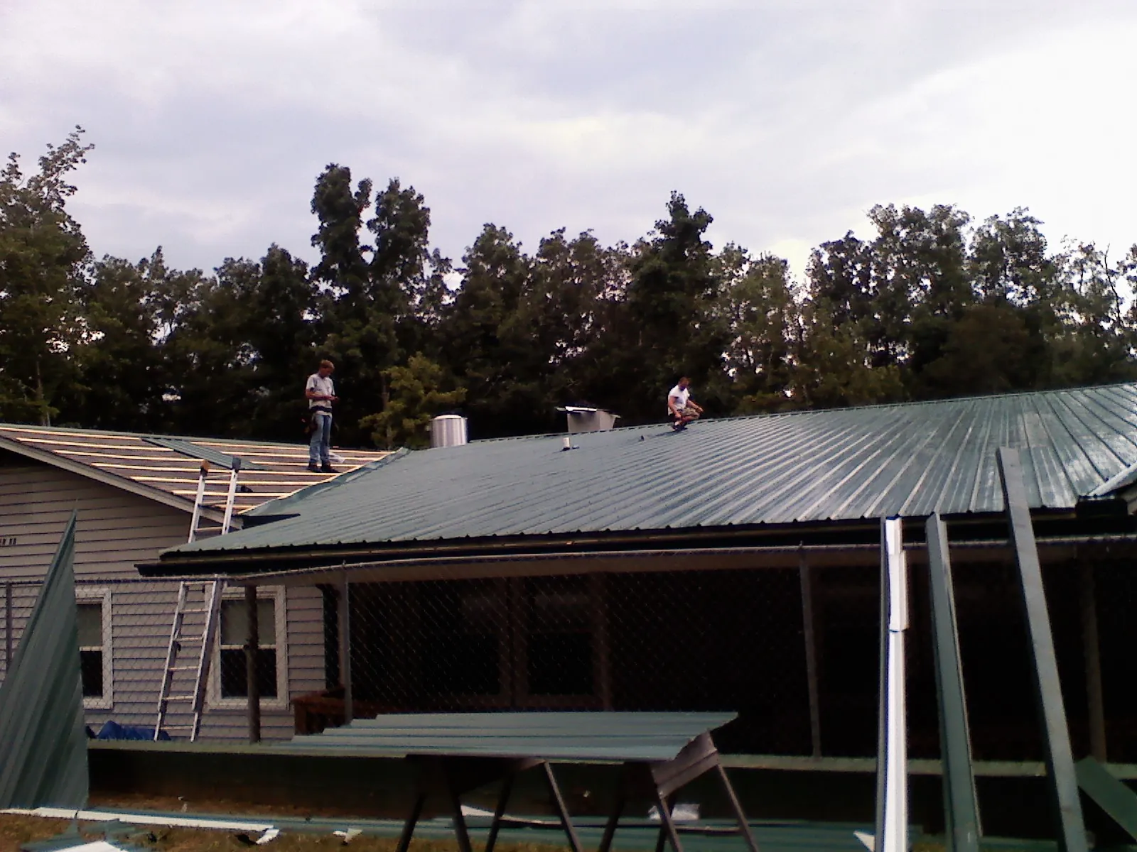 Two roofers installing green metal panels above a covered porch in Woodbridge