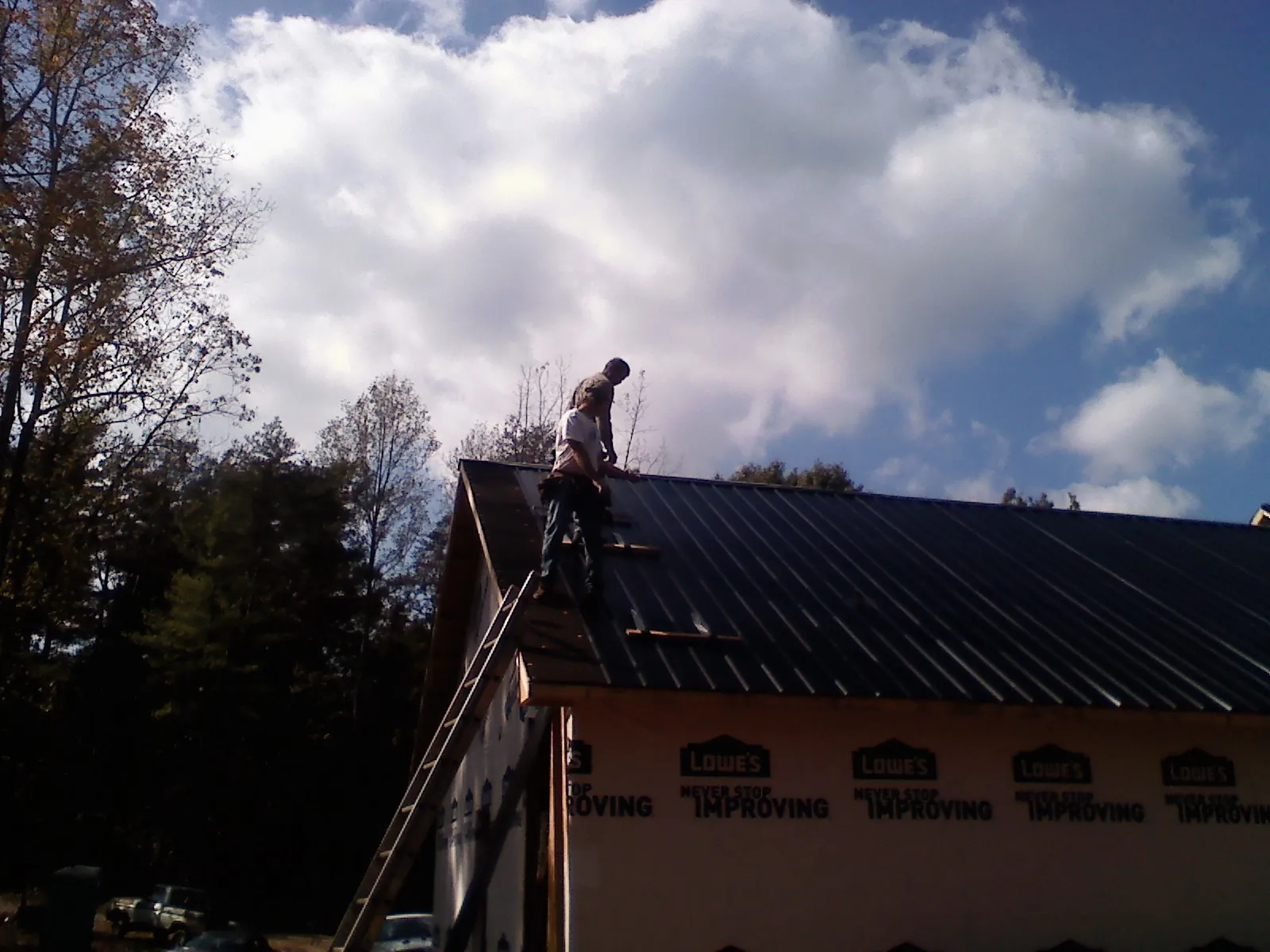 Roofer fastening dark metal panels high against a cloudy sky, from a Roof Inspection job in Woodbridge