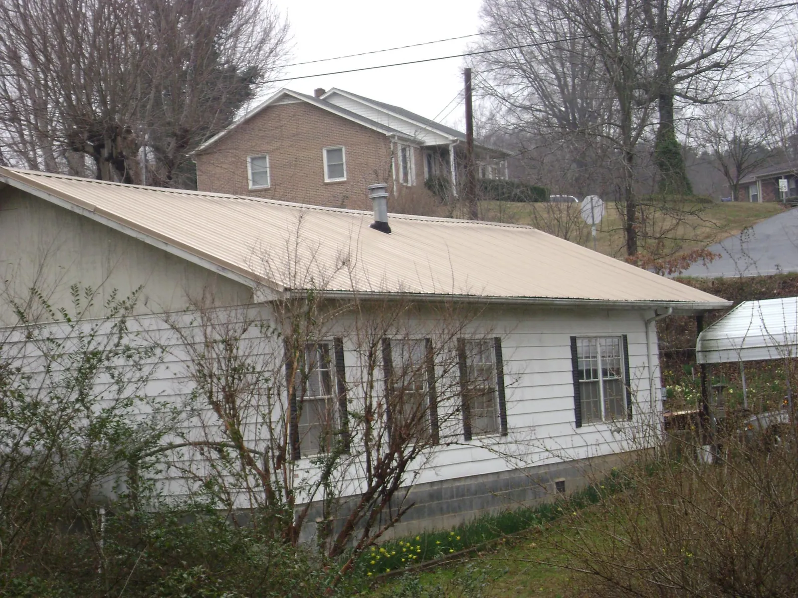 Tan metal roof on a white sided house set into a hillside — Commercial Roofing by Roofing Brothers in Woodbridge